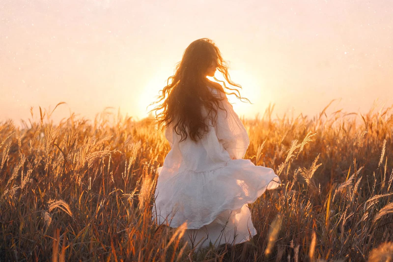 A young woman in a white linen dress standing in a field of tall grass at golden hour, backlit, hair moving in the wind, film grain, soft focus, romantic and airy.