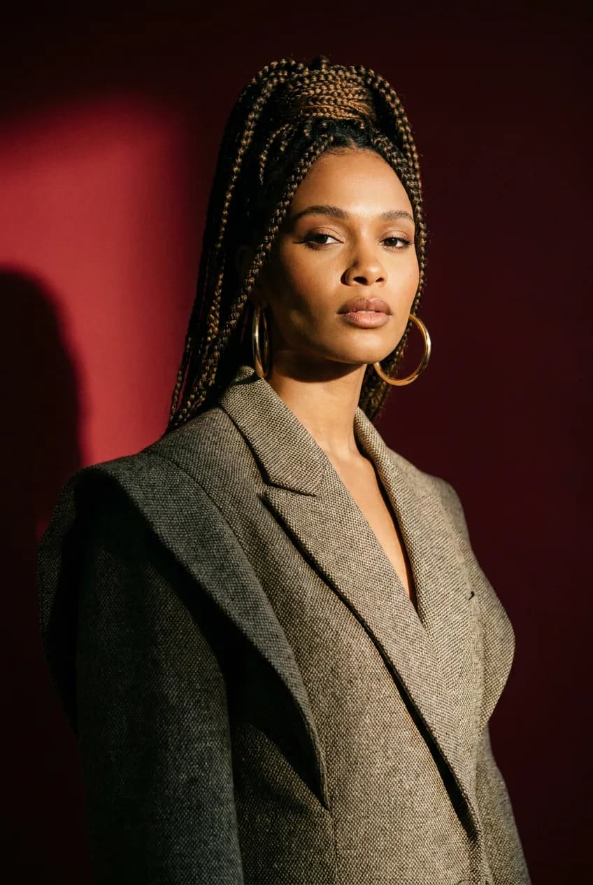 Studio fashion portrait of a woman with braided hair and gold hoop earrings, deep red backdrop, dramatic side light, editorial, Hasselblad look.
